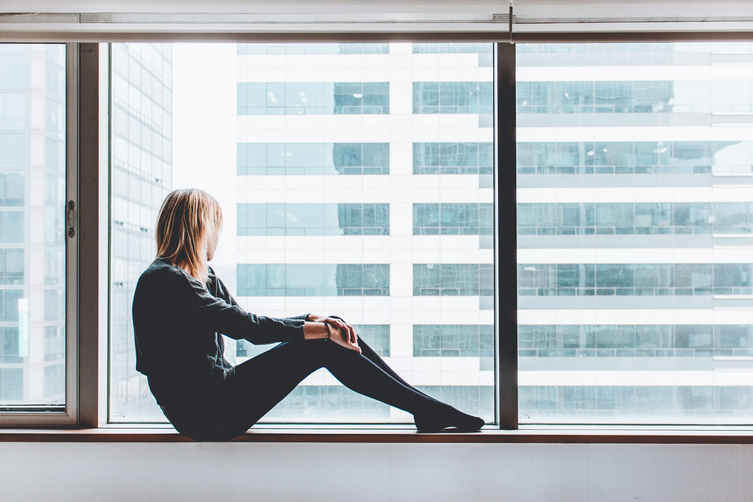 Jeune femme de dos regardant par la fenêtre d'un immeuble de bureau